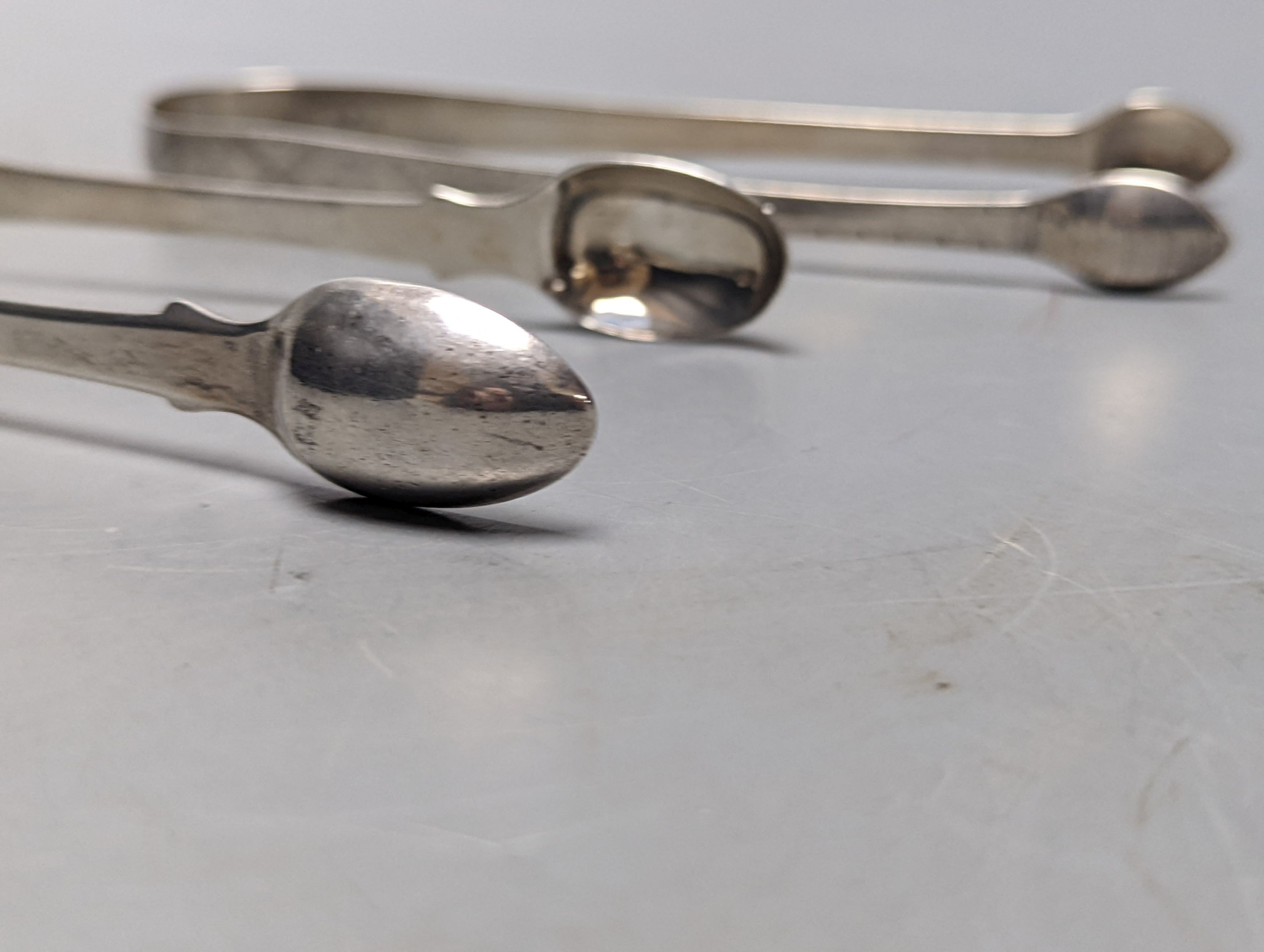 Two pairs of George III bright cut engraved silver sugar tongs and a pair of George IV silver sugar tongs, various dates and makers